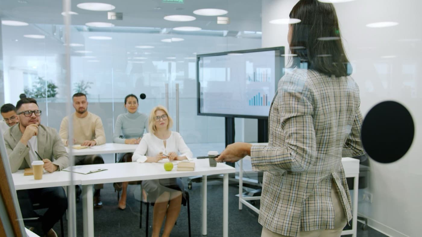 Professional handing a certification document across a desk to a manager, with an email draft visible on a laptop